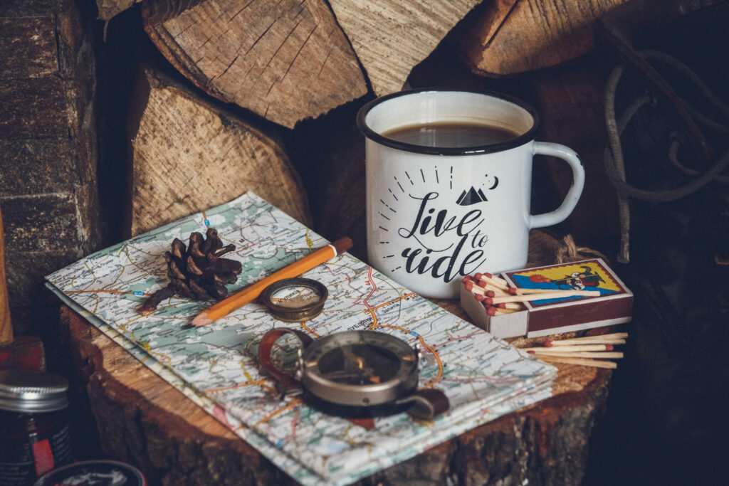 Une image esthétique contenant une tasse de café, une carte, une boussole, posés sur des rondins de bois